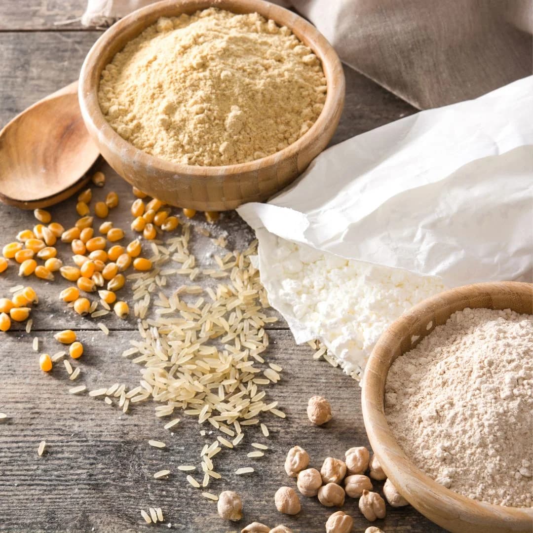 Bowls of rice flour, chickpea flour, and corn flour placed on a wooden table