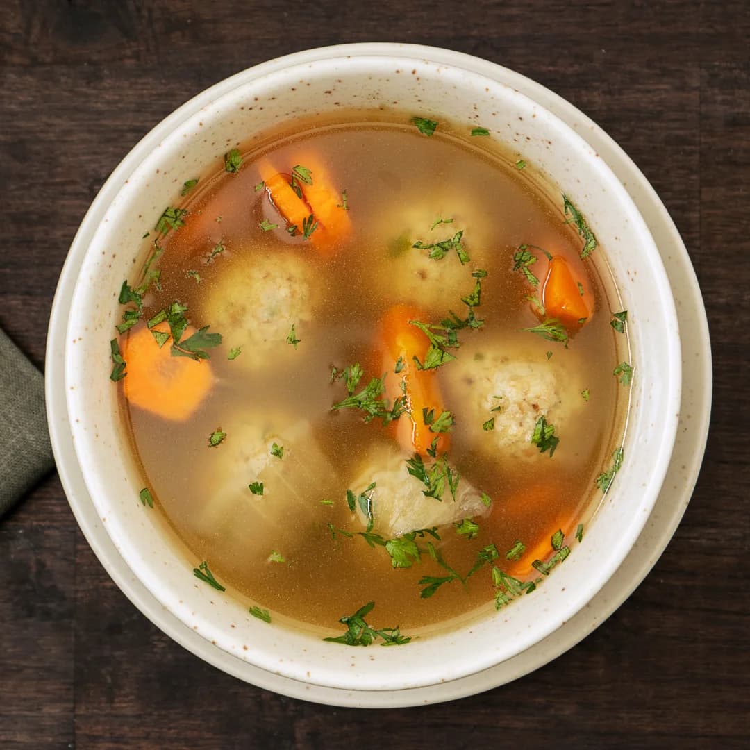 Top view of carrot and cabbage soup garnished with oregano, served in a white bowl on a wooden table.