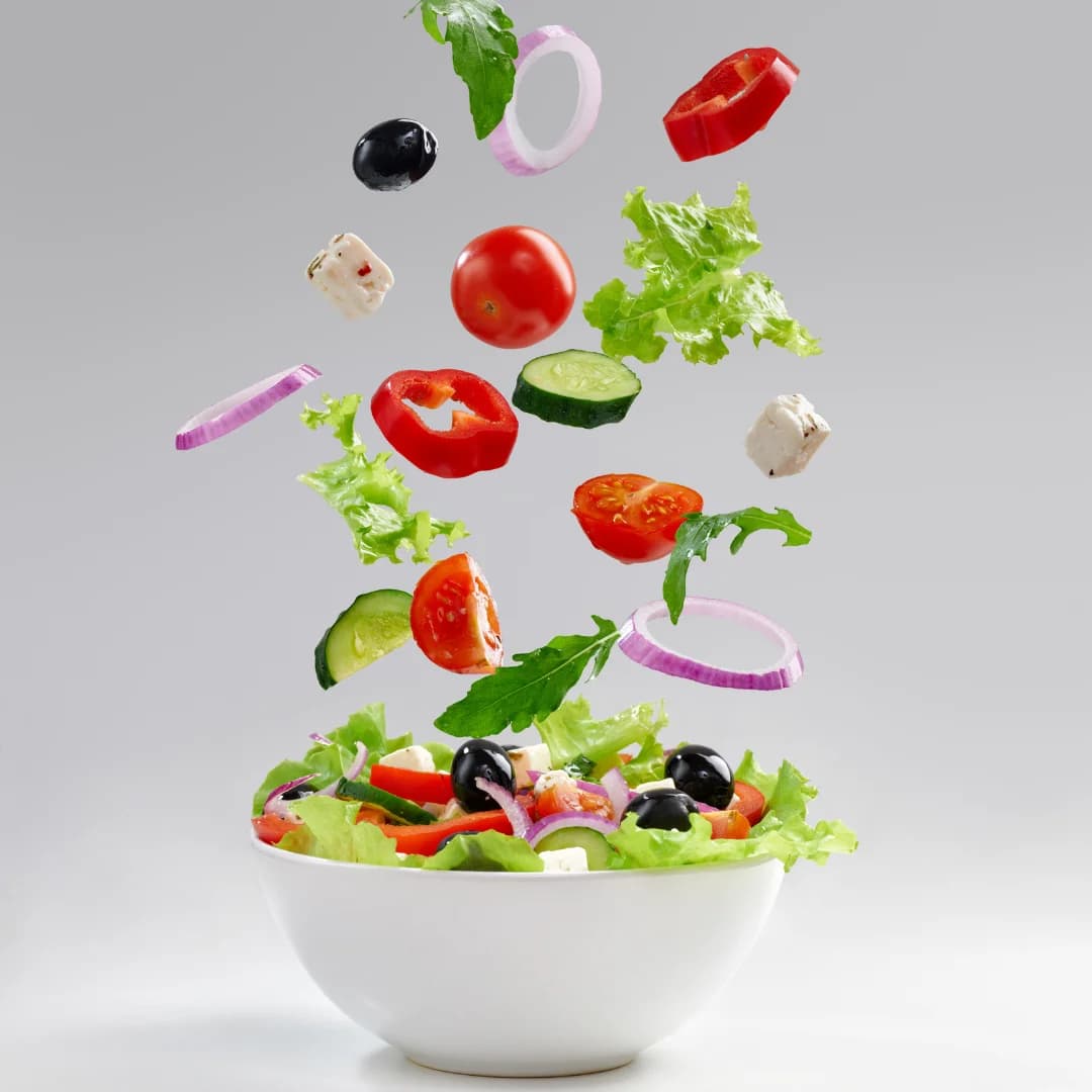 front view a white bowl of salad with vegetables lettuce, onions, black olives, tomatoes