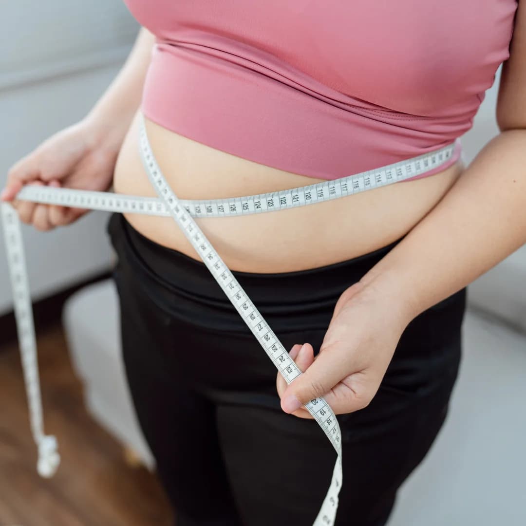 Top view of a woman measuring her belly with inch tape at home