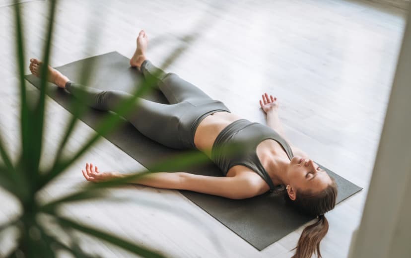 a lady doing Corpse Pose of yoga on yoga mat in the house morning view